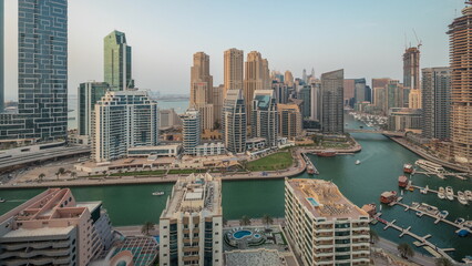 Fototapeta premium Panorama showing Dubai Marina with several boat and yachts parked in harbor and skyscrapers around canal aerial timelapse.