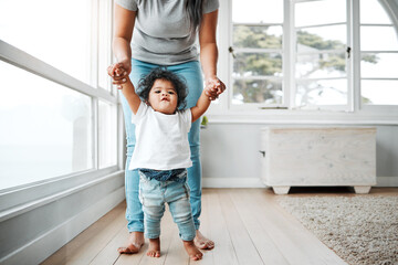 Watching her take her first steps. Shot of a little girl learning to walk with the help of her...