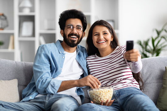Smiling interracial spouses sitting on couch at home, watching tv