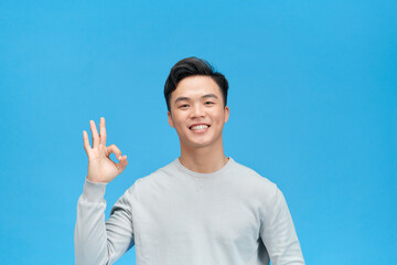 Portrait of handsome man showing ok sign and smiling isolated over blue background