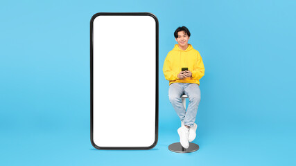 Asian Teen Guy Sitting Near Big Phone Screen, Blue Background