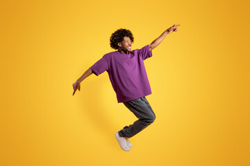 Fototapeta na wymiar Cheerful adult african american curly man in purple t-shirt dancing, has fun alone