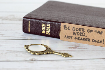 Be doer of the Word, not hearer only, handwritten verse with closed holy bible book and antique golden mirror on wood. A closeup. James 1:22 Scripture, obedience to God Jesus Christ, Christian concept - obrazy, fototapety, plakaty