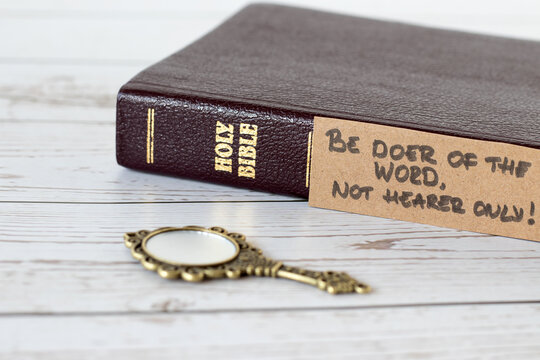 Be doer of the Word, not hearer only, handwritten verse with closed holy bible book and antique golden mirror on wood. A closeup. James 1:22 Scripture, obedience to God Jesus Christ, Christian concept