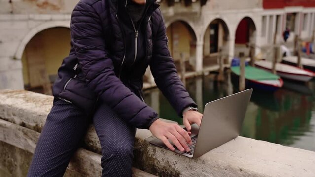 Man with mustache works on laptop sitting on bridge parapet