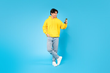 Fototapeta na wymiar Korean Teen Boy Using Cellphone Standing Over Blue Background