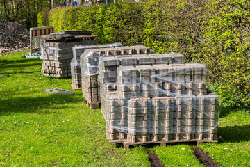 Gray road tiles stacked on pallets covered with polyethylene film. Standing on a green lawn. - Powered by Adobe