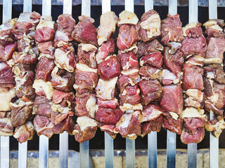 Appetizing shashlik skewers with raw lamb on grill, top view