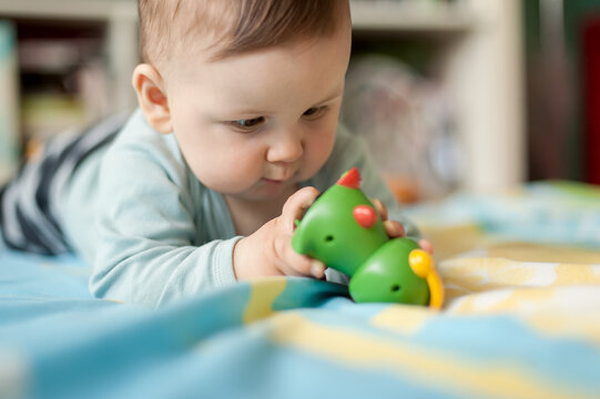 Portrait of cute baby boy playing with colorful toys at home while lies on its stomach. Playground for babies