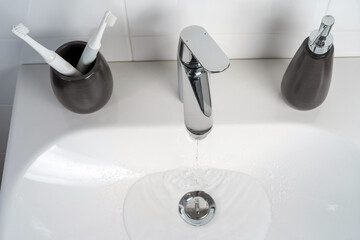 A jet of clean water flows from a faucet into a white sink. Selective focus.