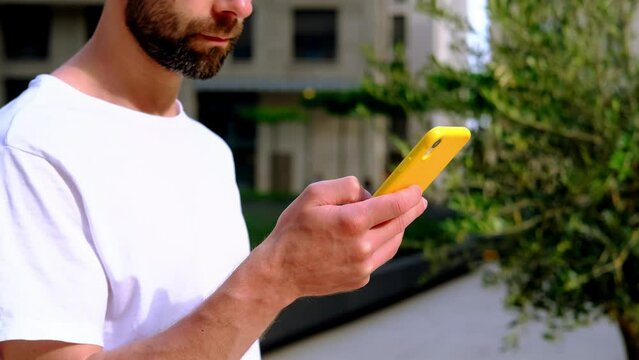 bearded young man using phone in yellow case in modern city, using phone in city, beautiful blurred background, Telecommunication with friends, technology in everyday, Banking and Investment