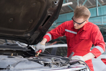 Fototapeta na wymiar Car mechanic service, repair, maintenance concept. Male mechanic working and using jumper cables for charger car battery in auto repair shop. Male mechanic worker inspecting car electric in garage