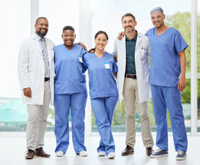 Fototapeta premium Together they save lives. Shot of a cheerful group of doctors standing with their arms around each other inside of a hospital during the day.