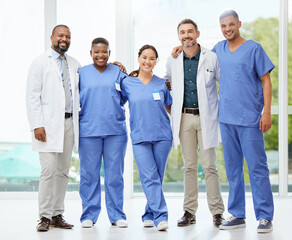 Together they save lives. Shot of a cheerful group of doctors standing with their arms around each other inside of a hospital during the day.