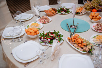 Table setting for the holiday. Round table with salads and sliced rolls, appetizers, bread.