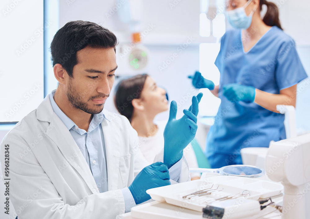 Poster Deep in through during the selection process. Shot of a dentist applying his gloves while selecting the tool he needs.