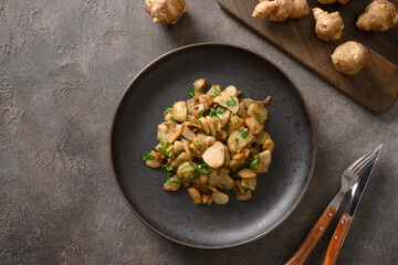 Roasted Jerusalem artichoke root, topinambur, sunchokes with parsley on brown background. Top view....