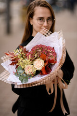 Young woman holding big and beautiful autumn style bouquet of fresh flovers and oak leaves