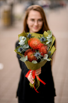 Young florist girl gives to cameraman bouquet of beautiful thistle, leucospermum, eucalyptus.
