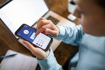 Young adult woman using a banking app on her phone while working from home