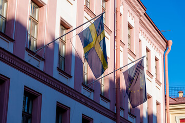 Close-up view of Swedish and EU flags fluttering on pink building wall in the early morning. Clear blue sky. Soft focus. Travel in Scandinavia theme. - obrazy, fototapety, plakaty