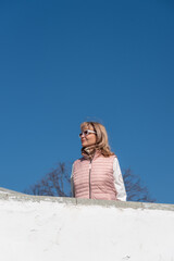 Beautiful adult woman in sunglasses with blond hair on the stairs against a blue clear sky.
