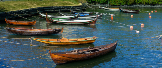 A group of long, skinny, colorful boats tied up to shore and anchored to buoys in Stockholm Sweden.