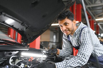 Fototapeta na wymiar latin hispanic auto mechanic in uniform is examining a car while working in auto service