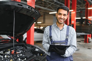 Indian car mechanic standing and working in service station. Car specialists examining the lifted...
