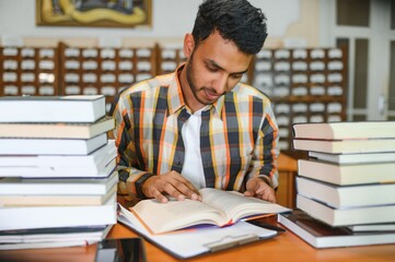 Male indian student at the library with book