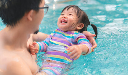 Asian little baby girl swimming in pool, Father holding daughter for safety support, Living lifestyle family indoors concept.