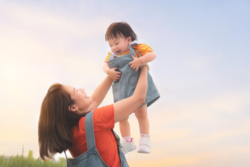 Happy Asian mother plays with daughter and holding girl in hands at park with nice sky, Baby smile...