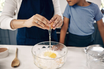 Closeup of female hands cracking a egg into a bowl while baking at home with her son. Woman adding...