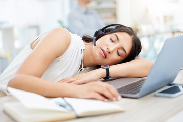 Overworked and in need of a break. Shot of a young call centre agent sleeping at her desk in an office.