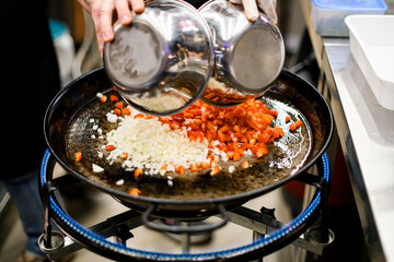 Chef pours out chopped pepper and onion on pan. Fire burns under the pan.