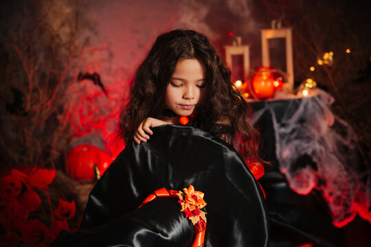 Little girl in a black dress and a hat in the image of a witch for halloween.