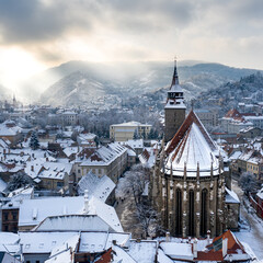 Black Church with snowy roof in Brasov Transylvania with sun rays escaping from the clouds in the...