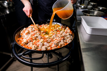 Chef adding tomato water to rice, meat and vegetables in frying pan