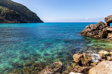 A beautiful landscape of the coast of the island of Corfu in the Ionian Sea of the Mediterranean in Greece. Pure blue clear water washes over the shores of the Greek island.