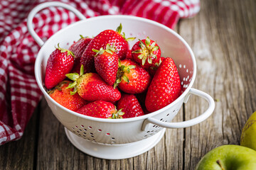 Strawberries in white colander placed on a rustic wooden background. Fresh and tasty seasonal ripe and fruit.