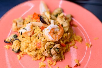 Traditional Spanish dish Paella with meat, rice , seafood on pink plate