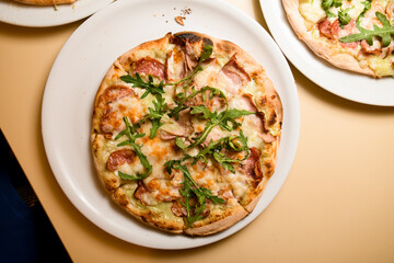 Three ready-made mini pizzas with jamon,ruccola covered with cheese on light table