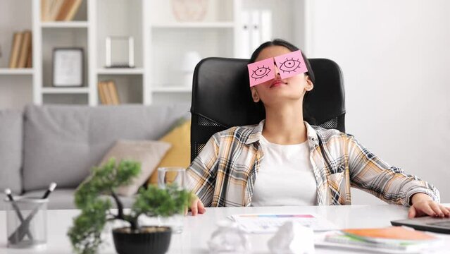 The concept of a lot of work. Tired Indian student girl sleeping with stickers on her eyes while sitting at the table. Distracted woman in home office.