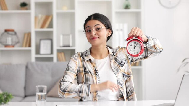 Indian smiling woman showing time on clock, approving, pointing finger at clock, encouraging. This is your time.