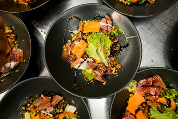 Top view on plates with tasty and healthy salad with jamon, salad mix, cheese, nuts and terijaki sause .
