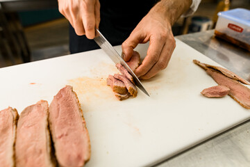 Close-up photo of a chef hands slicing baked meat on white kitchen board