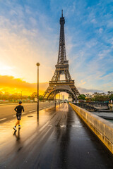 Young man run on the bridge at sunrise time after rain. Morning jogging under Eiffel Tower in...