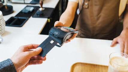Close up of barista holding credit card swipe machine while customer making payment by card