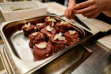 Chef put cloves of garlic on raw beef pieces in steel baking form