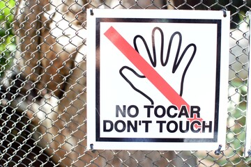 A sign with a crossed hand hanging on a metal grid informing about the prohibition of touching